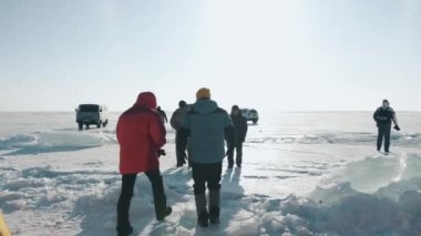 Baykal, Irkutsk Bölgesi, Rusya - 18 Mart 2021: Erkekler, güneşli bir günde donmuş Baykal Gölü 'nde buz kütleleri ve karların arasında UAZ minibüslerinin arka planına karşı dururlar