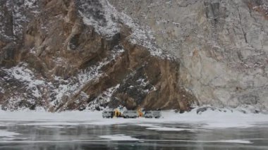 Baykal, Irkutsk Bölgesi, Rusya - 18 Mart 2021: UAZ minibüsleri ve bir grup insan Olkhon Adası 'nın kayalık dağlarının arka planına karşı Baykal Gölü' nün buzunda kamp kurdular.
