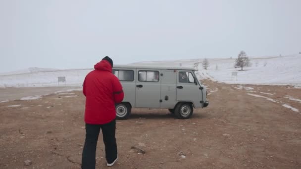 Um homem de casaco vermelho de inverno vai e senta-se em uma excursão UAZ para uma viagem ao Lago Baikal. Visão traseira — Vídeo de Stock