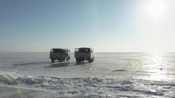 Dwa minibusy UAZ stoją na lśniącym lodzie jeziora Bajkał na tle błękitnego, czystego nieba — Wideo stockowe