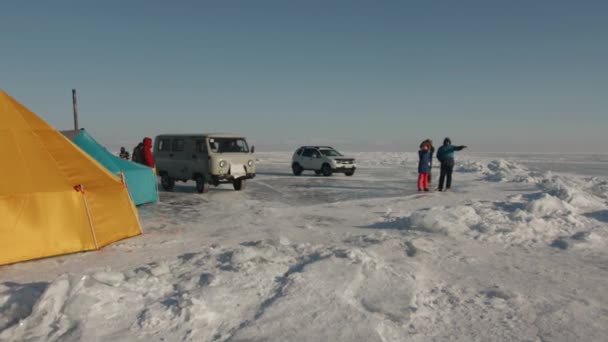 Baikal, Irkutsk Region, Russia - March 18, 2021: Μια ομάδα ανθρώπων σε ένα στρατόπεδο σκηνή στην παγωμένη λίμνη Baikal και μικρά λεωφορεία UAZ παράδοση τουριστών στον προορισμό τους — Αρχείο Βίντεο
