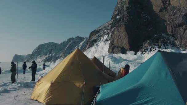 Baikal, Gebiet Irkutsk, Russland - 18. März 2021: Eine Gruppe von Menschen zeltet in einem Zelt auf dem Eis des Baikalsees vor dem Hintergrund der Felsen der Insel Olchon — Stockvideo