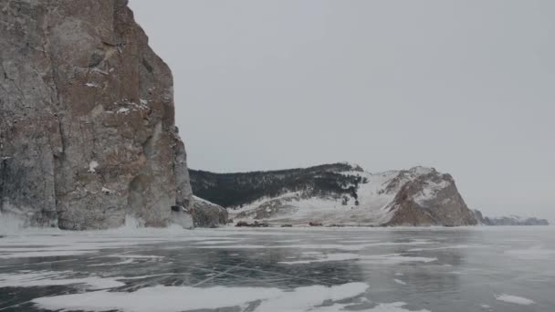 Fantastisk utsikt över steniga berg vid kusten av frusna sjön Baikal och bilar med människor på is — Stockvideo