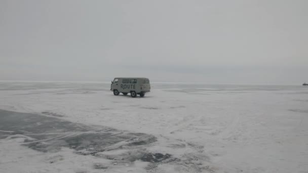 Baikal, regione di Irkutsk, Russia - 18 marzo 2021: i minibus UAZ trasportano le persone attraverso il ghiaccio ghiacciato del lago Baikal oltre le montagne rocciose sulla costa — Video Stock