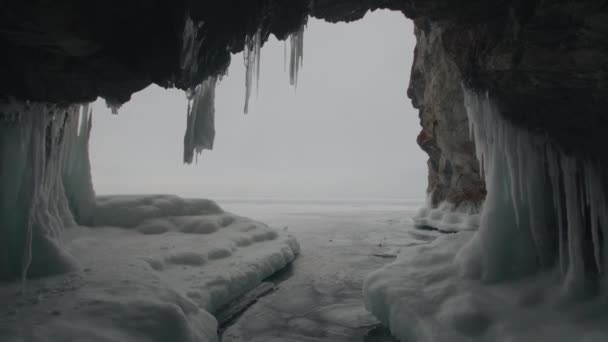 Blick aus der Eishöhle mit Eiszapfen an der Decke und Wänden und Eis am Boden auf den zugefrorenen Baikalsee — Stockvideo