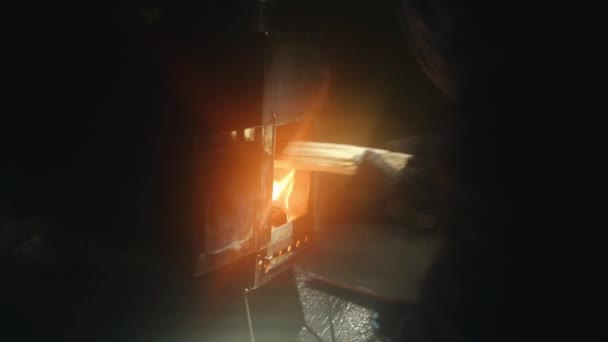 Mężczyzna w rękawiczkach kładzie drewno na ogień w metalowym piecu w ciemnym pokoju. Zbliżenie — Wideo stockowe