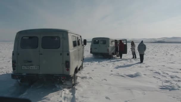Baikal, obwód irkucki, Rosja - 18 marca 2021 r.: Grupa turystów wsiada do minibusów UAZ na pokrytym śniegiem lodzie jeziora Bajkał z widokiem na pasma górskie na wybrzeżu — Wideo stockowe