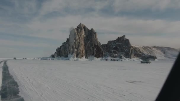 Una vista dal finestrino della macchina sulle rocce sulla riva del lago ghiacciato Baikal e un gruppo di persone e auto ai piedi — Video Stock