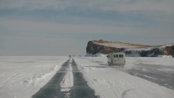 看到UAZ小型客车沿着冻结的贝加尔湖行驶，以及人们和汽车在悬崖下的海岸 — 图库视频影像