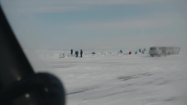 Baikal, obwód irkucki, Rosja - 18 marca 2021: Turyści spacerują wśród niebiesko-białych bloków lodu po zamarzniętym jeziorze Bajkał i kolumna minibusów UAZ stojących na drodze — Wideo stockowe
