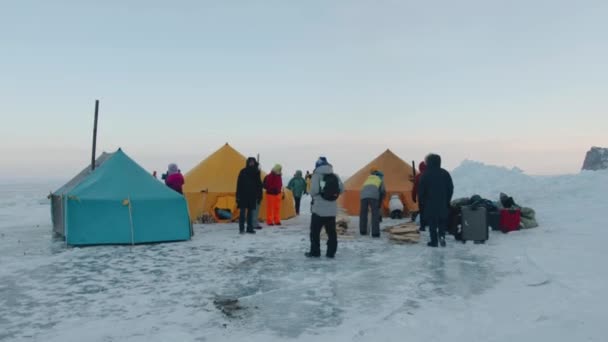 Baikal, Irkutsk Region, Ryssland - 18 mars 2021: En grupp turister i ett tältläger på den frusna isen vid sjön Baikal vid foten av den klippiga ön Olkhon — Stockvideo