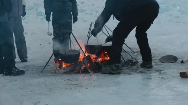 Toeristen koken eten in een pot boven een vuur in een tentenkamp aan het bevroren Baikalmeer. Langzame beweging — Stockvideo