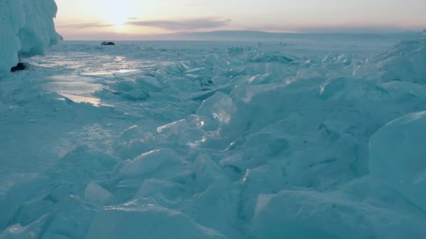 Modrobílé bloky průhledného ledu na zamrzlém jezeře Bajkal se třpytí v paprscích západu slunce a stojí v dálkových vozech — Stock video