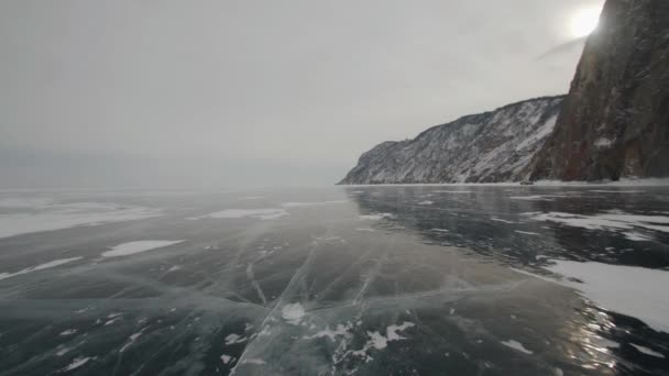 Winterlandschap met bergen tegen de achtergrond van de zon die door de wolken en auto 's breekt op het transparante ijs van het Baikalmeer — Stockvideo