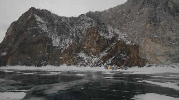 Baikal, Región de Irkutsk, Rusia - 18 de marzo de 2021: Tienda de campaña y minibuses UAZ al pie del acantilado de la isla de Olkhon en la costa del lago congelado Baikal — Vídeos de Stock