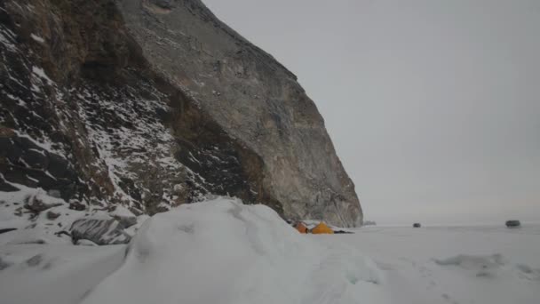 Minibusy UAZ i grupa ludzi w obozie namiotowym na przezroczystym lodzie jeziora Bajkał u podnóża skalistej góry — Wideo stockowe