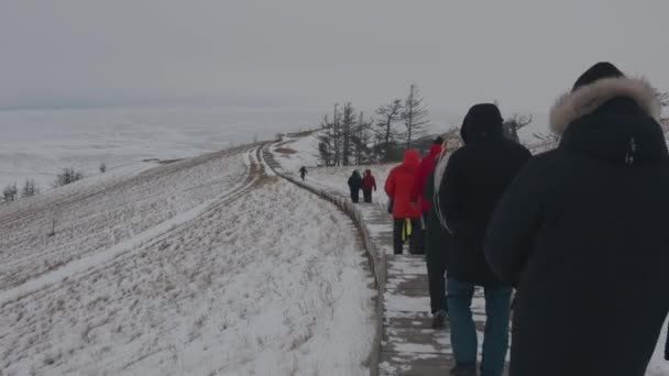 Baikal, Irkutsk Region, Ryssland - 18 mars 2021: En grupp turister går nedför en trätrappa från kullen och leder till den frusna sjön Baikal — Stockvideo