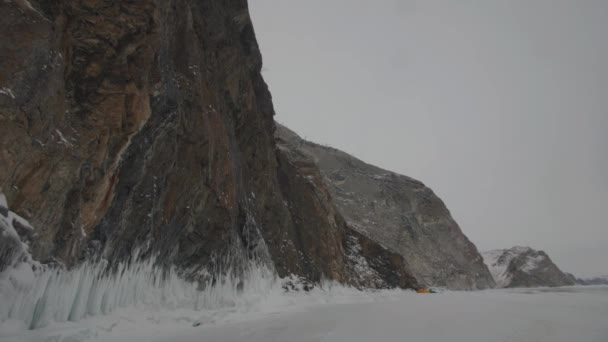 View of the rocky mountains on the coast of the frozen Lake Baikal and the tent camp at the foot of the cliff — Stock Video