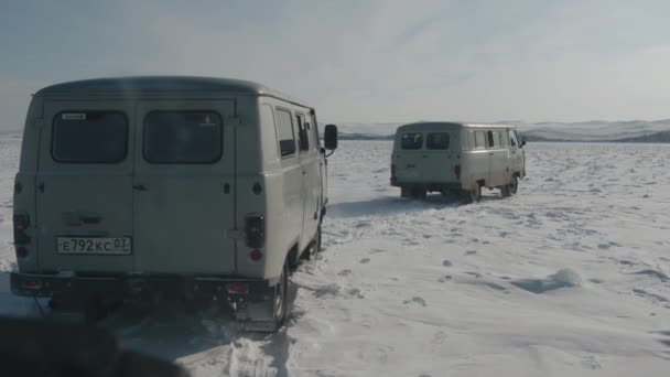 Baikal, obwód irkucki, Rosja - 18 marca 2021 r.: Minibusy UAZ przewożą turystów wzdłuż pokrytego śniegiem wybrzeża zamarzniętego jeziora Bajkał w słoneczny zimowy dzień. Zwolniony ruch — Wideo stockowe