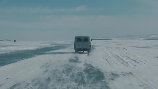 Вид через лобовое стекло автомобиля на конвой микроавтобусов УАЗ по ледяной дороге озера Байкал под ясным солнечным небом — стоковое видео