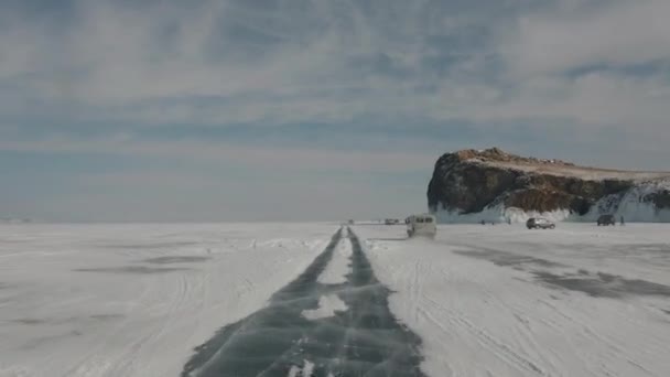 Kilátás az UAZ minibuszra, amely a befagyott Bajkál-tó mentén halad, valamint az emberekre és autókra a szikla lábánál a parton. — Stock videók