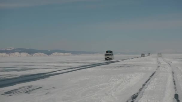 Drukke verkeer op het ijs van het Baikalmeer en een UAZ minibus met toeristen bezittingen geladen op het dak — Stockvideo