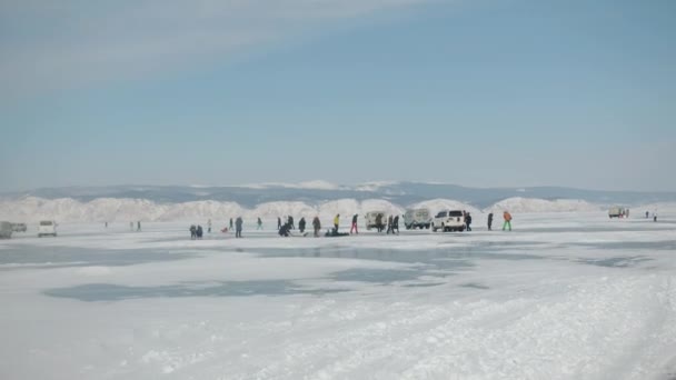 Gruppi di turisti camminano accanto alle auto e ammirano il ghiaccio trasparente unico del lago Baikal in una giornata di sole luminoso — Video Stock