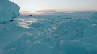 Donmuş Baykal Gölü 'nde gün batımında mavi şeffaf buz blokları ve uzaktaki turist gruplarıyla dolu arabalar.