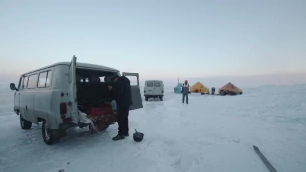 Baikal, região de Irkutsk, Rússia - 18 de março de 2021: miniautocarros UAZ e turistas em um acampamento de tenda no gelo congelado do Lago Baikal. Viagem de inverno extrema — Vídeo de Stock