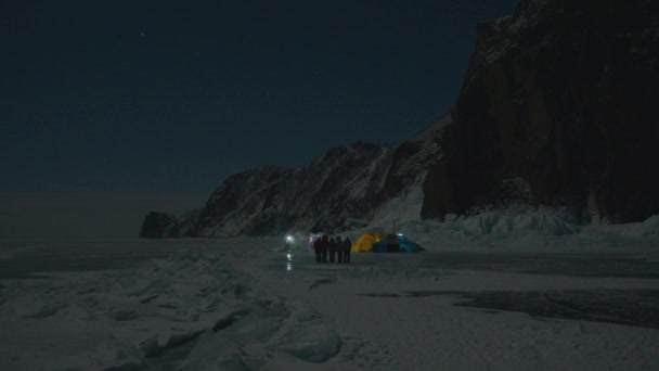 Een groep toeristen met zaklampen in hun handen staat 's nachts in de buurt van de tenten op het ijs van het Baikalmeer in de buurt van de rots. — Stockvideo