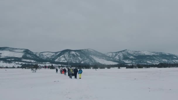 Baikal, Irkutsk Region, Ryssland - 18 mars 2021: En grupp turister går på en vintervandring på den frusna sjön Baikal mot bakgrund av snötäckta berg — Stockvideo