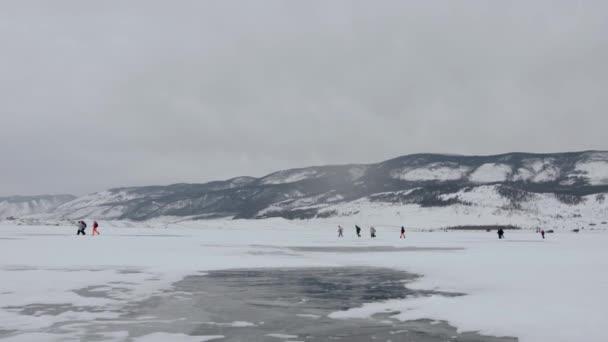 Een groep toeristen maakt een wandeling over het bevroren Baikalmeer tegen de achtergrond van bergen aan de kust — Stockvideo