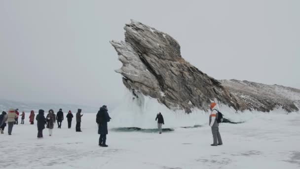 Baikal, Irkutsk Region, Russia - March 18, 2021: Dragon Rock on Lake Baikal. A group of men and women walks along the frozen Lake Baikal and are photographed near a rock covered with ice splashes — Vídeos de Stock