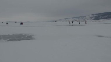 Bir grup turist, Baykal Gölü 'nün karlı buzunda arka plandaki kayalara doğru peş peşe gidiyor.