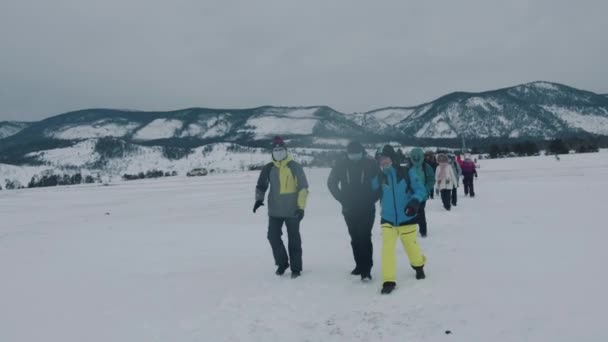 Bajkal, Irkutsk Region, Rusko - 18. března 2021: Skupina turistů jde ve sloupci přes zasněžené pole na pozadí podhůří jezera Bajkal a mává rukama — Stock video