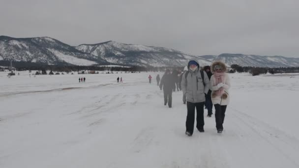 Baikal, região de Irkutsk, Rússia - 18 de março de 2021: Um grupo de homens e mulheres em casacos de inverno caminham no lago congelado Baikal. Movimento lento — Vídeo de Stock