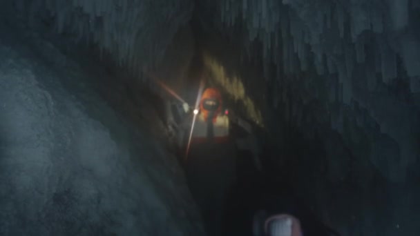 Байкал, Иркутская область, Россия - 18 марта 2021 года: группа туристов пробирается через ледяную пещеру с сосульками и освещает дорогу фонариками на телефонах — стоковое видео