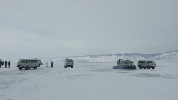 Хивусское судно на воздушной подушке стоит на льду озера Байкал рядом с микроавтобусами УАЗ, перевозящими туристов между островами — стоковое видео