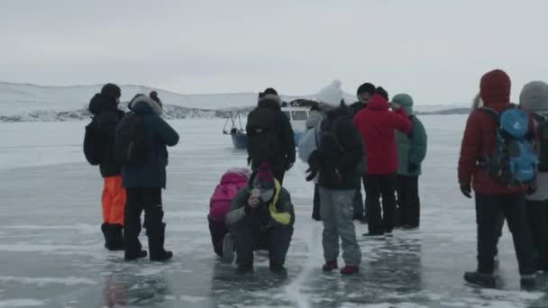 バイカル,イルクーツク地域,ロシア- 2021年3月18日:観光客のグループは、バイカル湖と通過ホバークラフトの透明な氷を調査し、写真を撮る — ストック動画