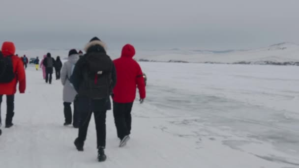 Baikal, Irkutsk Region, Russia - March 18, 2021: Large groups of tourists walk along the frozen Lake Baikal next to the road and cars passing on the ice. Slow motion — Vídeo de stock