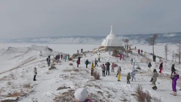 Baikal, Irkutsk Region, Ryssland - Mars 18, 2021: Många turister går på kullen Ogoy Island nära den buddhistiska stupa av upplysning och panorama av frusen Lake Baikal — Stockvideo