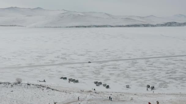 View from the mountain to the road with transport on the ice of Lake Baikal and many cars and tourists at the foot of the rocks — Vídeo de stock