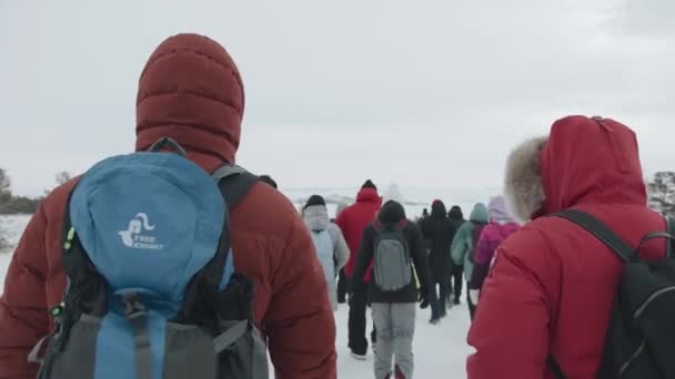 Baikal, Irkutsk Region, Ryssland - 18 mars 2021: En grupp turister med ryggsäckar gå längs en snötäckt väg när du reser längs sjön Baikal. Bakåt. Långsamma rörelser — Stockvideo