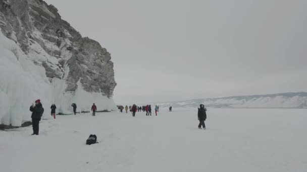 Baikal, regio Irkoetsk, Rusland - 18 maart 2021: Een groep toeristen reist langs het bevroren Baikalmeer en onderzoekt de grotten en rotsen bedekt met ijspegels op Olkhon Island — Stockvideo