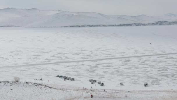 Panorama de la carretera en el lago congelado Baikal y un grupo de personas y coches al pie de la montaña. Movimiento lento — Vídeo de stock