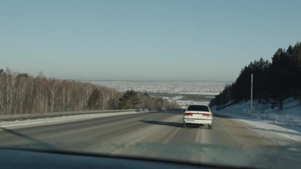 Regione di Irkutsk, Russia - 18 marzo 2021: Il movimento delle auto sulla strada principale circondato da una foresta fuori città e un panorama di un campo innevato — Video Stock