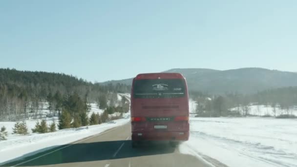 Baikal, regione di Irkutsk, Russia - 18 marzo 2021: un'auto sorpassa un autobus rosso su un'autostrada circondata da campi innevati e foreste sulle colline — Video Stock