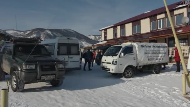 Baikal, Irkutsk Region, Rusko - 18. března 2021: Auta a skupina turistů na zasněžené ulici hotelového komplexu — Stock video