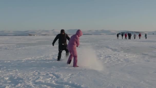 Un groupe de touristes se promène le long du lac Baïkal gelé et deux d'entre eux s'amusent et jettent la neige avec leurs pieds. Mouvement lent — Video