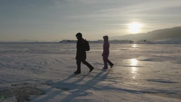 Un grupo de turistas camina sobre el hielo cubierto de nieve del lago Baikal al atardecer y una joven corre con los brazos extendidos — Vídeo de stock